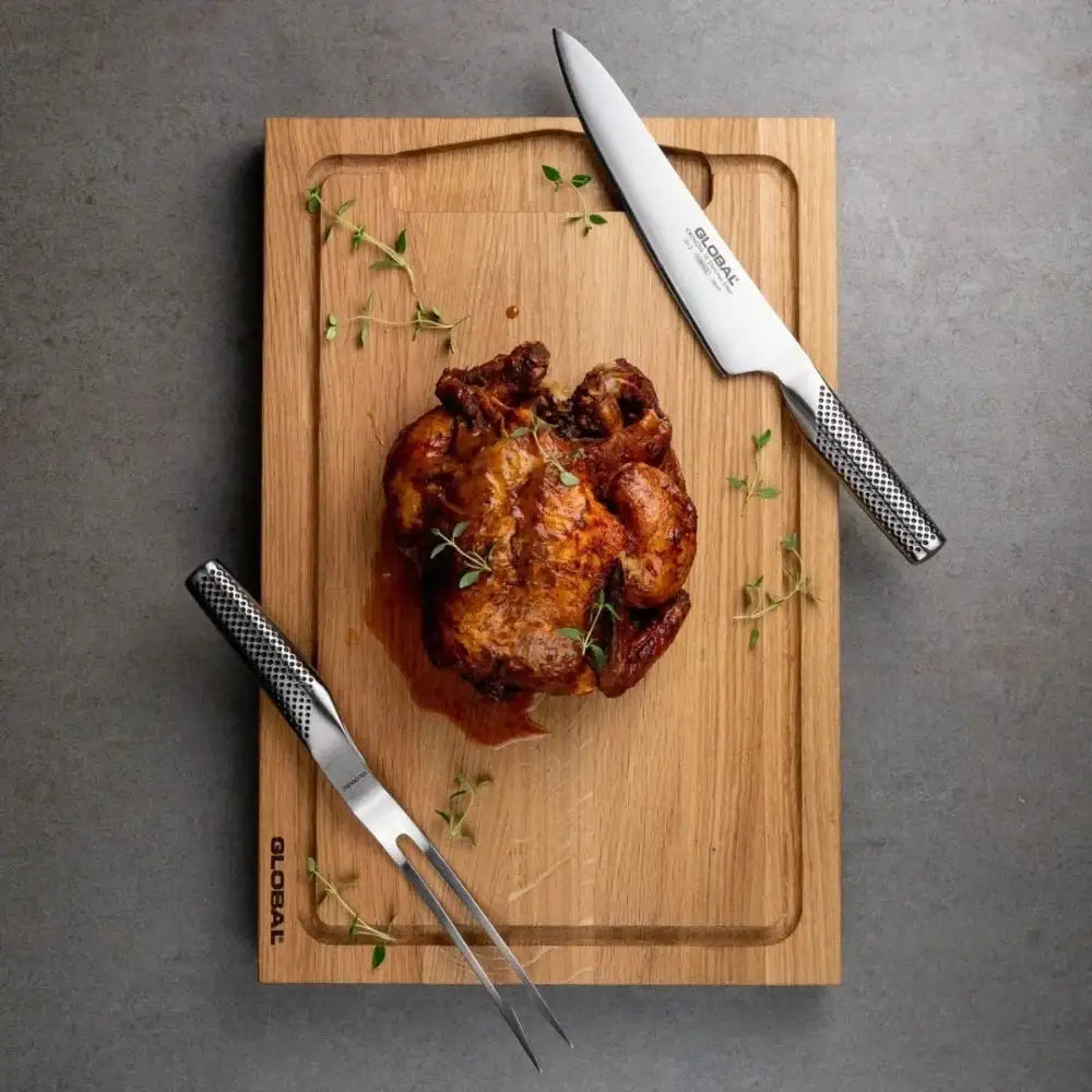 Roasted chicken on a wooden cutting board with two knives on a gray surface