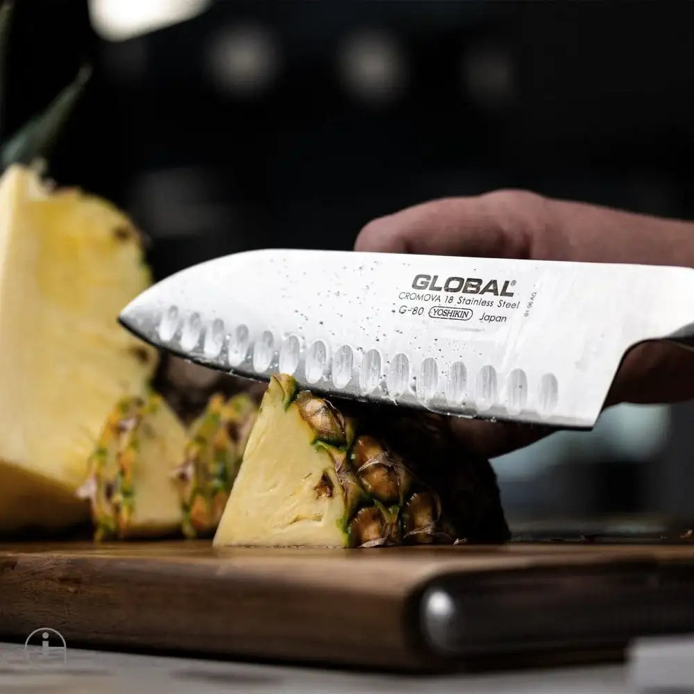Person using a Global brand knife to cut a pineapple on a wooden cutting board.