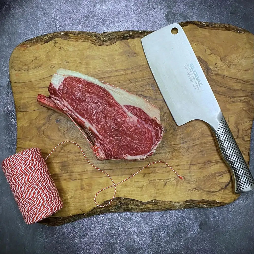 Raw steak on a wooden cutting board with a cleaver and twine.