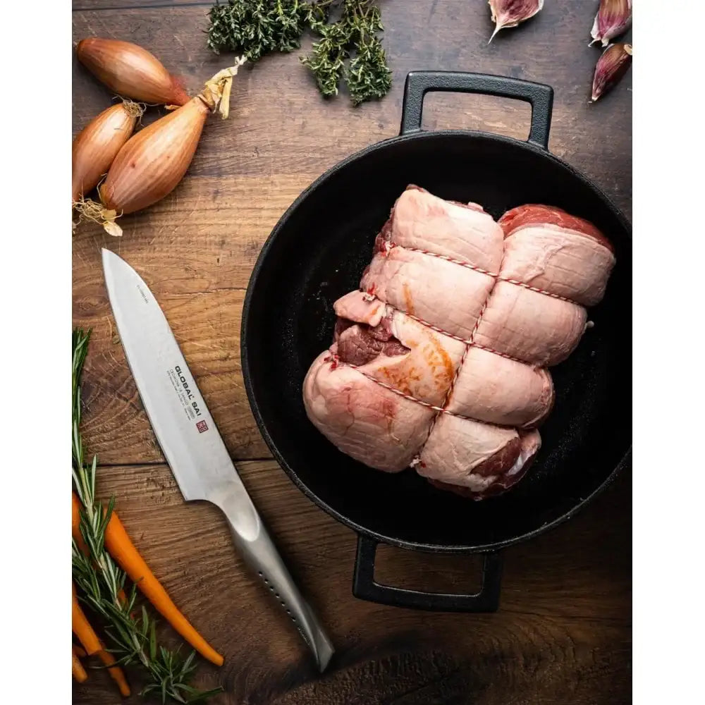 Raw pork belly in a black cast iron skillet on a wooden surface with a knife and herbs.