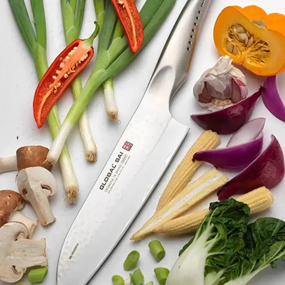 Knife with a brand label surrounded by various vegetables on a white surface