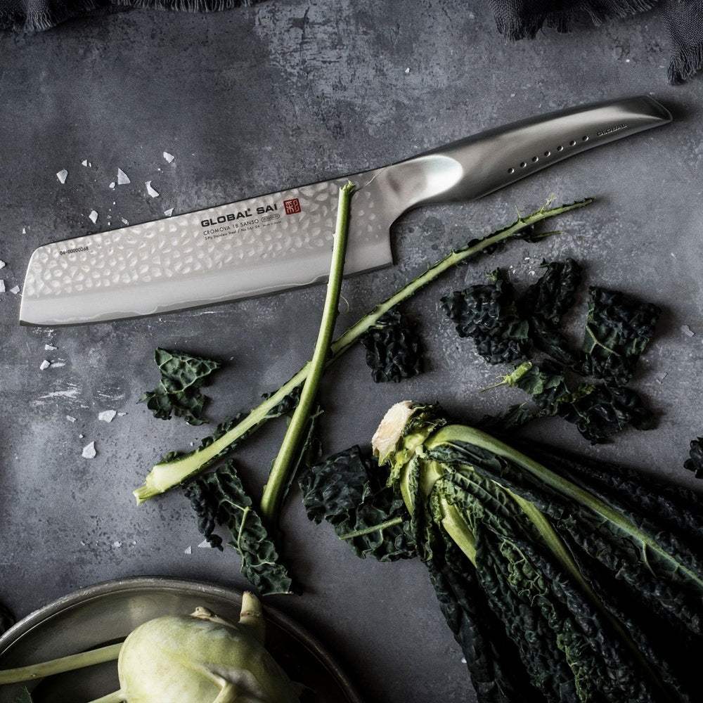 Knife with a textured blade on a dark surface with kale and kohlrabi.