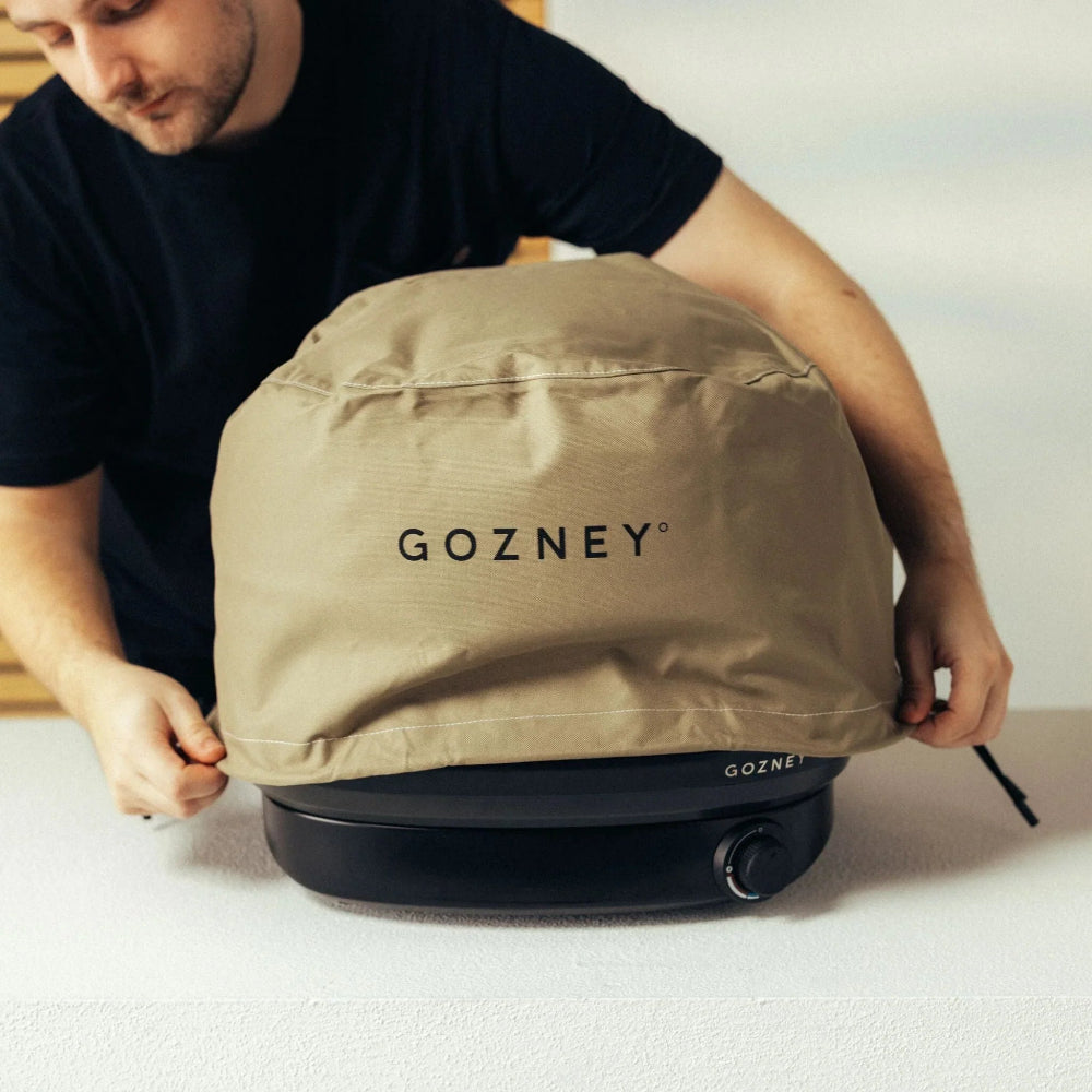 Person holding a tan Gozney branded cover over a stove.