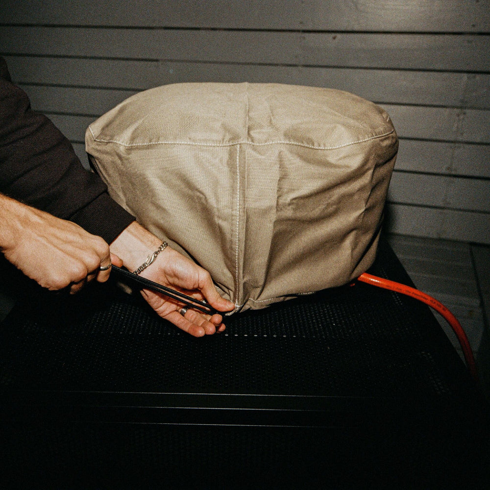 Person tying a beige pizza oven cover fabric bag with on a dark surface.