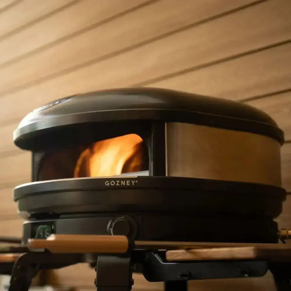 Gozney Arc XL 16 compact outdoor pizza oven in black with wood-fired flame, on patio at Cookin Stores