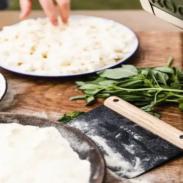 Gozney pizza dough cutter with flour, fresh herbs, and cheese on a kitchen prep table at Cookin Stores