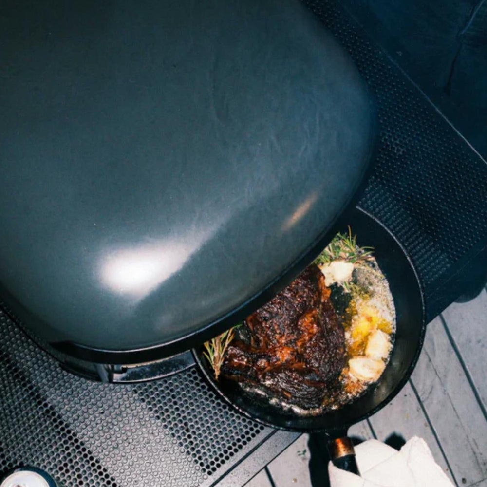 Person cooking food on a portable stove with a frying pan on a wooden floor.
