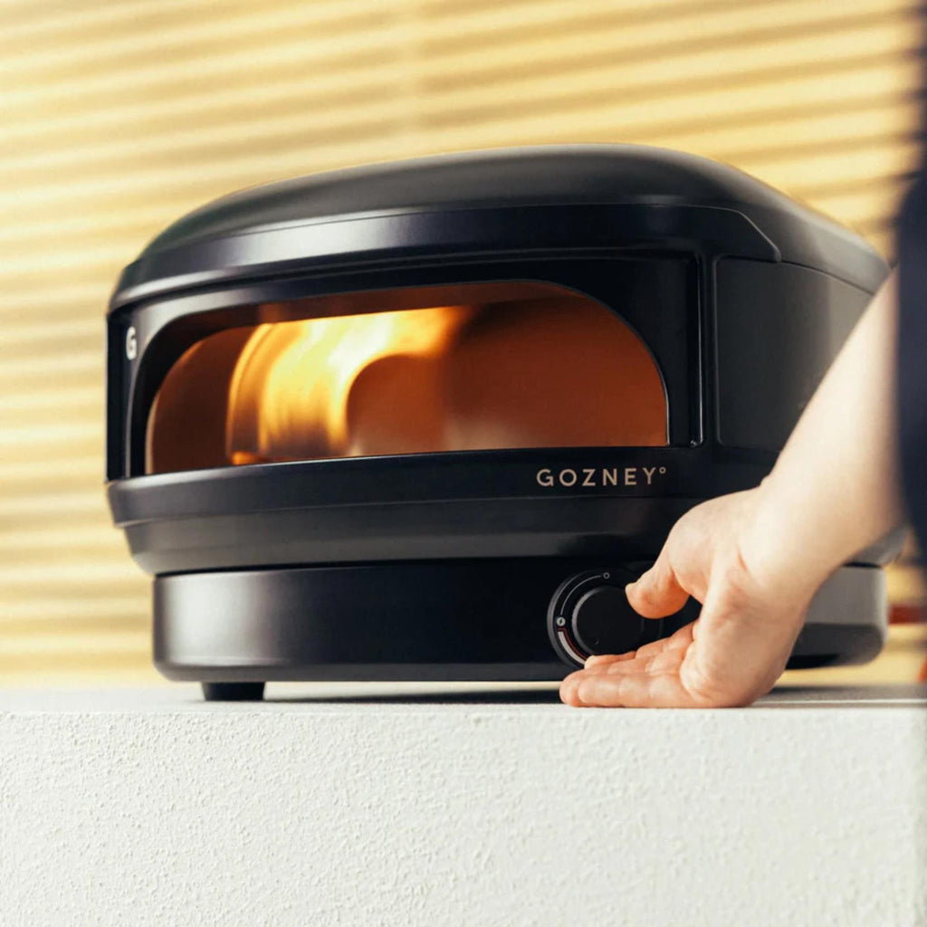 Gozney pizza oven with a hand adjusting the temperature dial on a light wood background