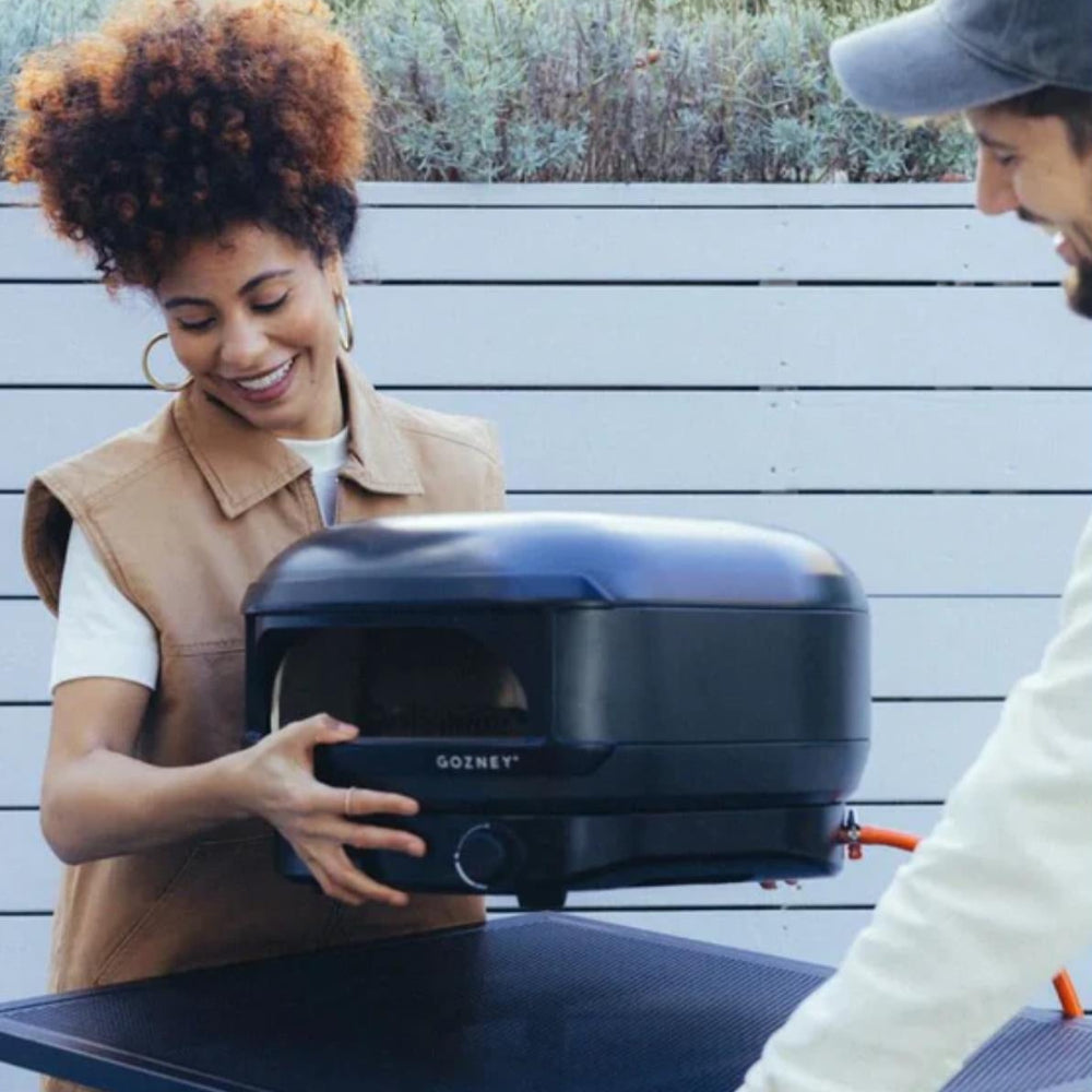 Two people outdoors, one holding a portable barbecue grill.