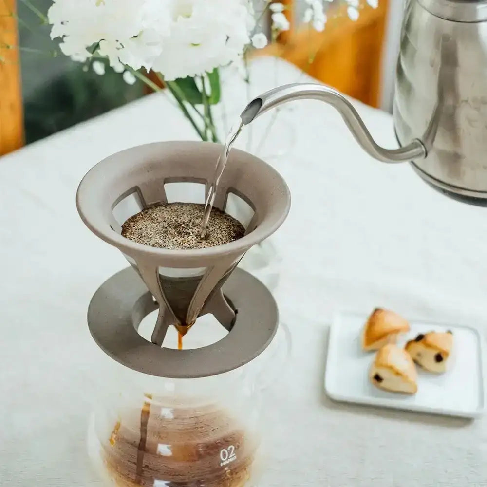 Coffee brewing process with a pour-over coffee maker on a table with a teapot and dessert.