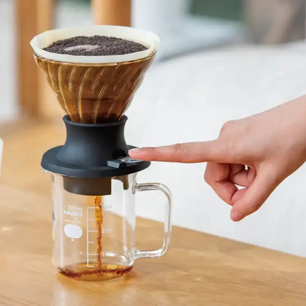 Hand using a coffee dripper to pour coffee into a glass mug on a wooden surface.
