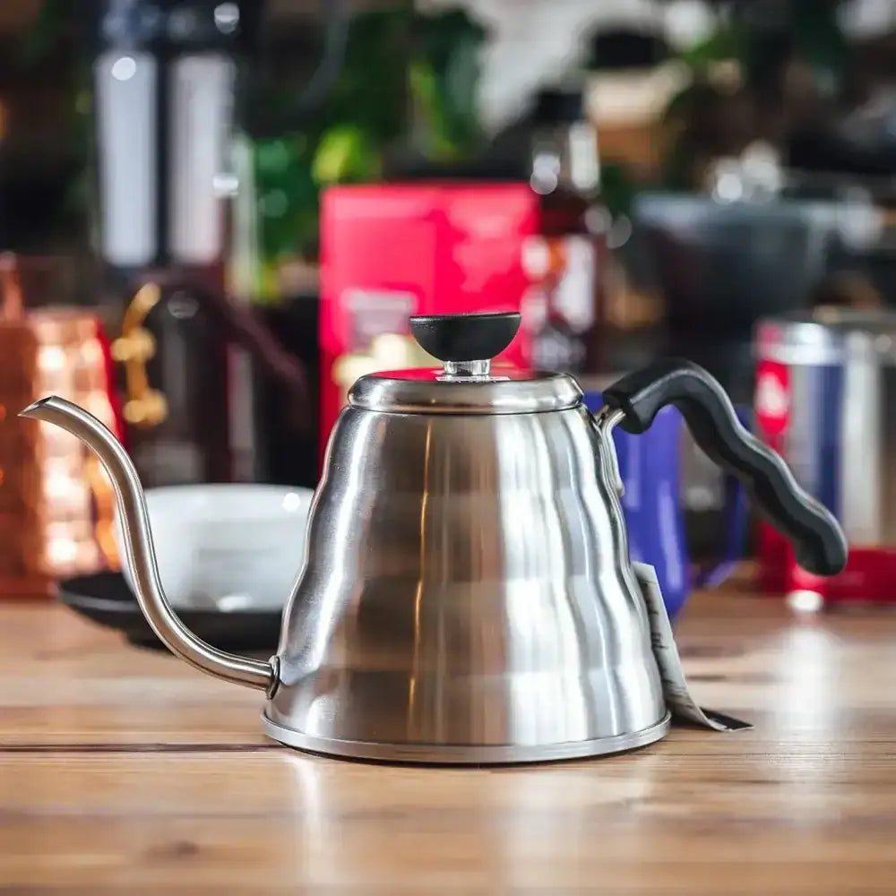 Stainless steel kettle on a wooden surface with a blurred coffee shop background