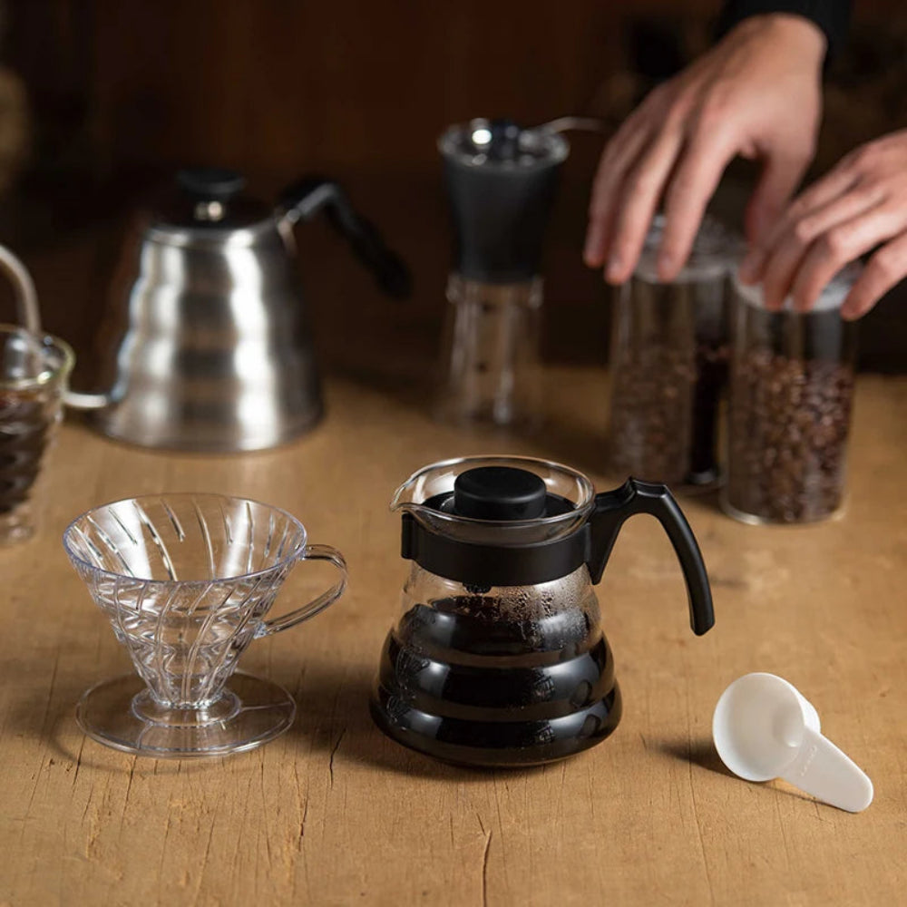 Coffee-making setup with a black coffee pot, clear filter, and glass carafe on a wooden surface.