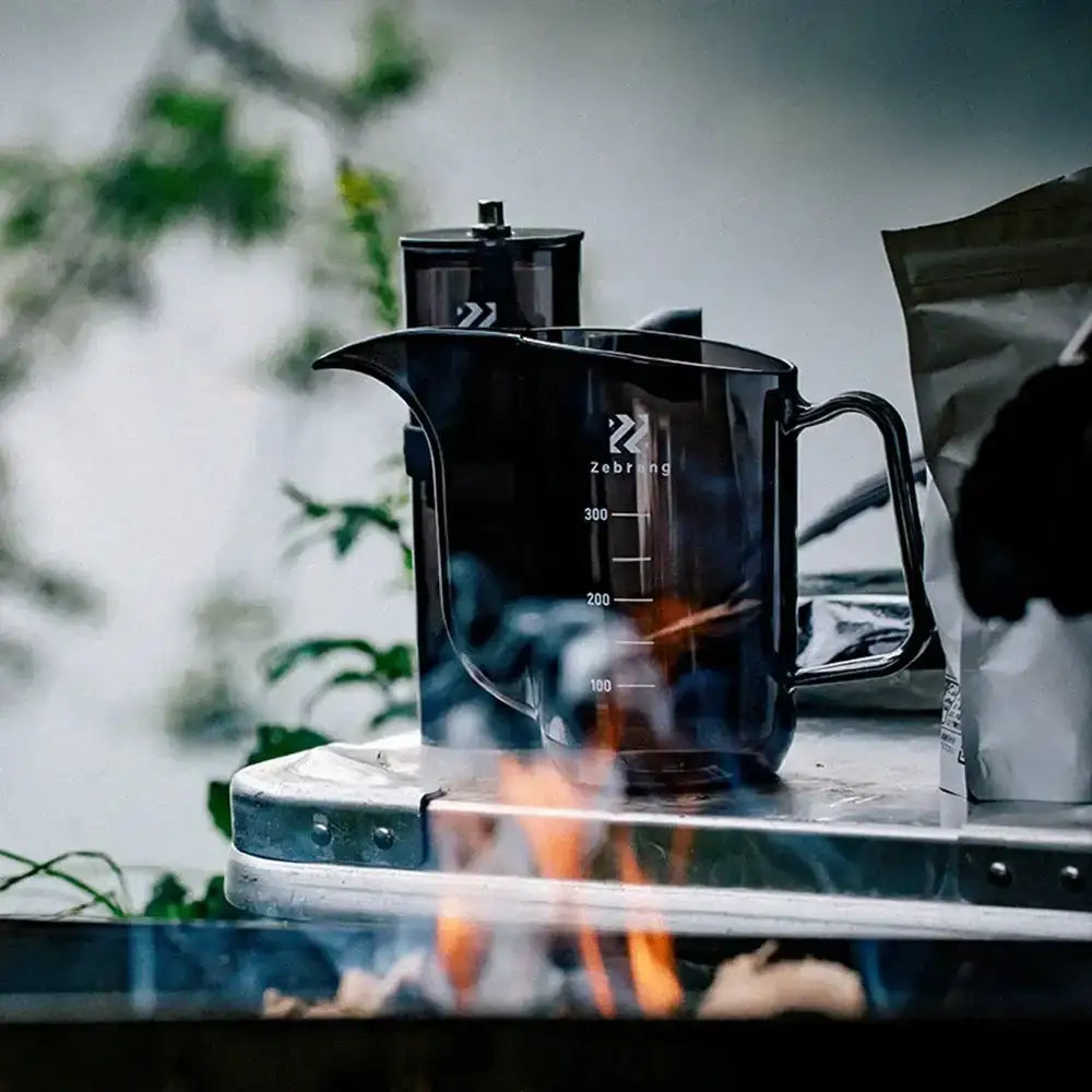 Black coffee maker on a camping stove with a blurred natural background