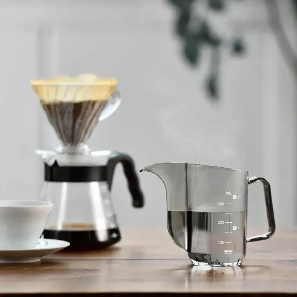 Coffee brewing setup with a pour-over coffee maker and glass measuring cup on a wooden surface.