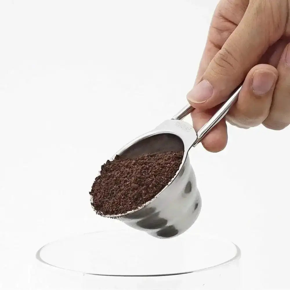 Hand holding a metal scoop filled with ground coffee on a white background