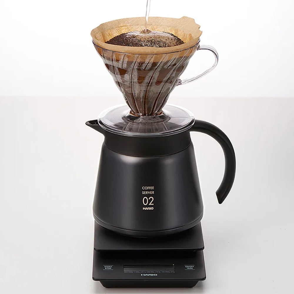 Black coffee server with a paper filter and coffee grounds on a white background