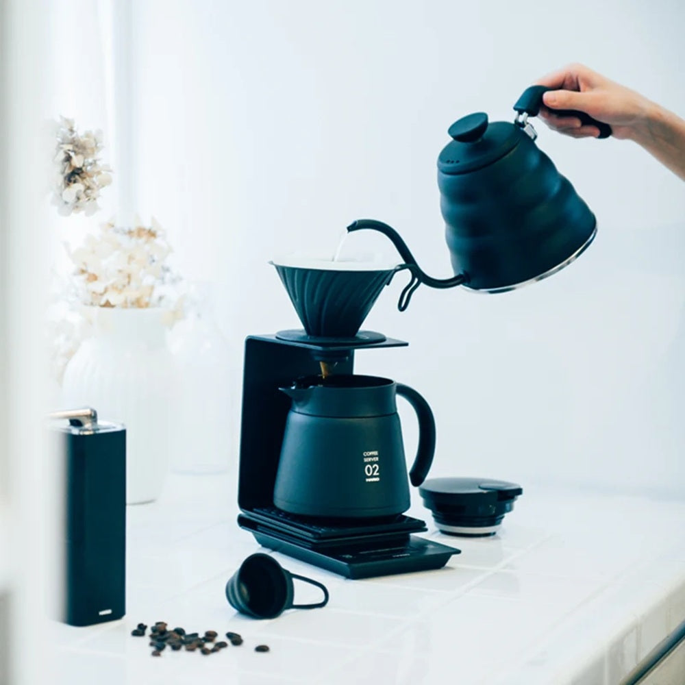 Person pouring coffee from a blue kettle into a coffee maker on a white countertop.