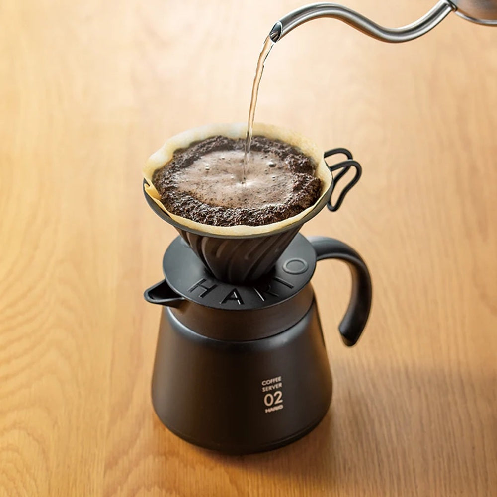 Coffee being poured into a Hario coffee maker on a wooden surface