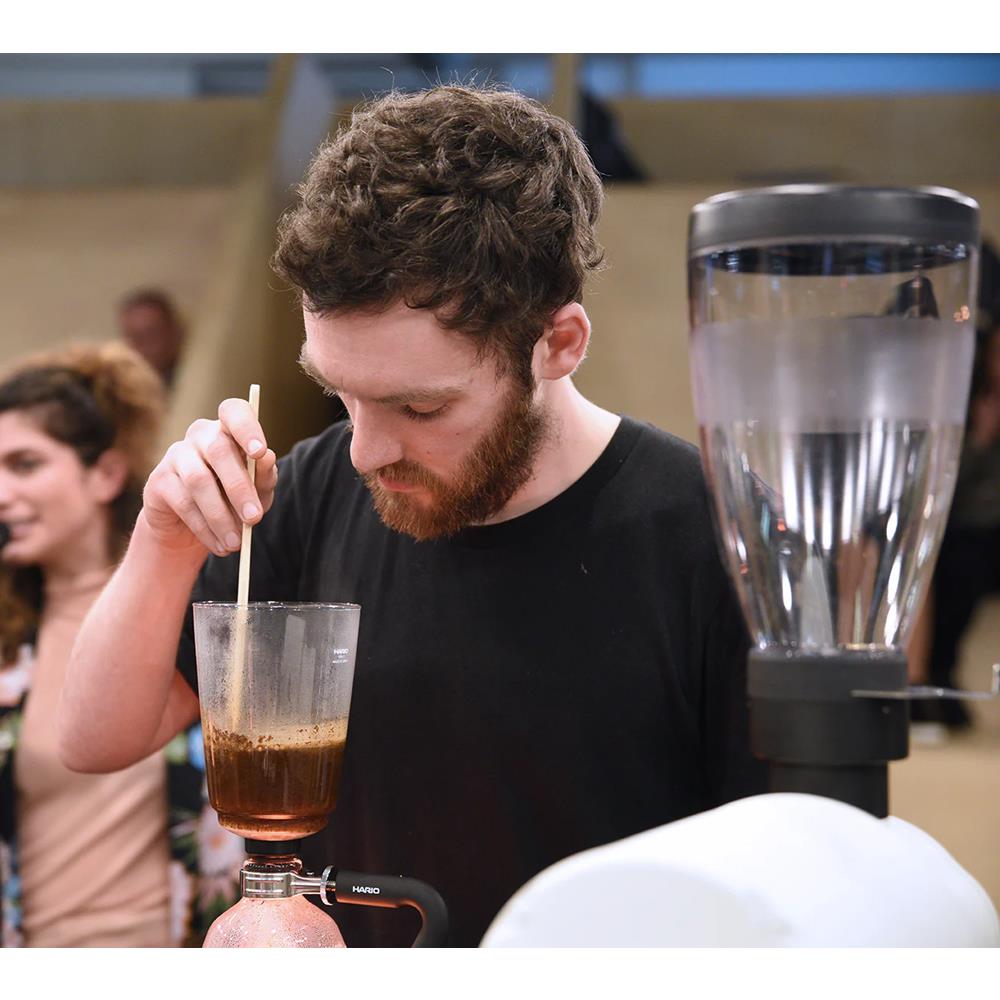 Man with a beard stirring a coffee drink in a bar setting