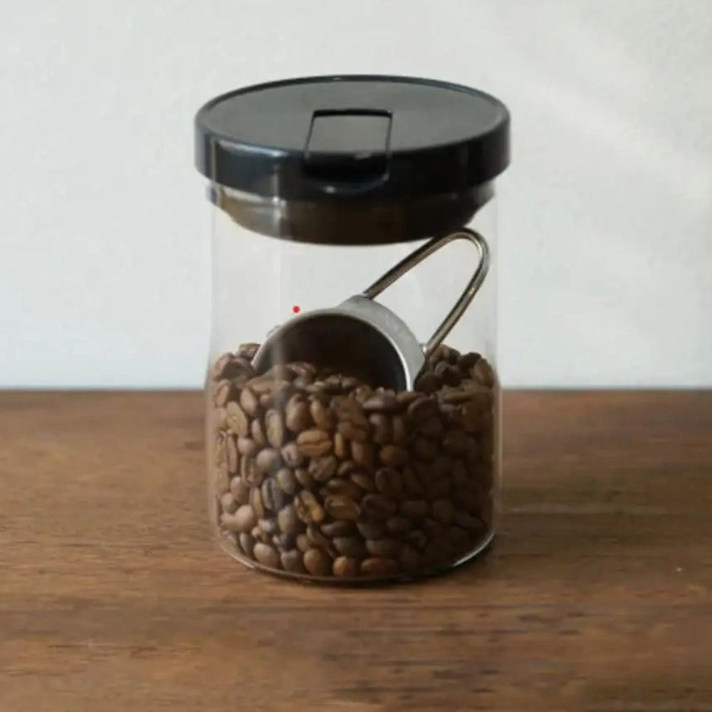Glass jar with black lid filled with coffee beans on a wooden surface.