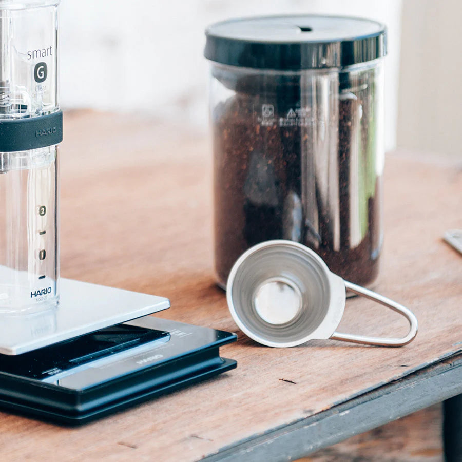 Coffee brewing equipment including a smart G coffee maker and a Hario coffee grinder on a wooden surface.