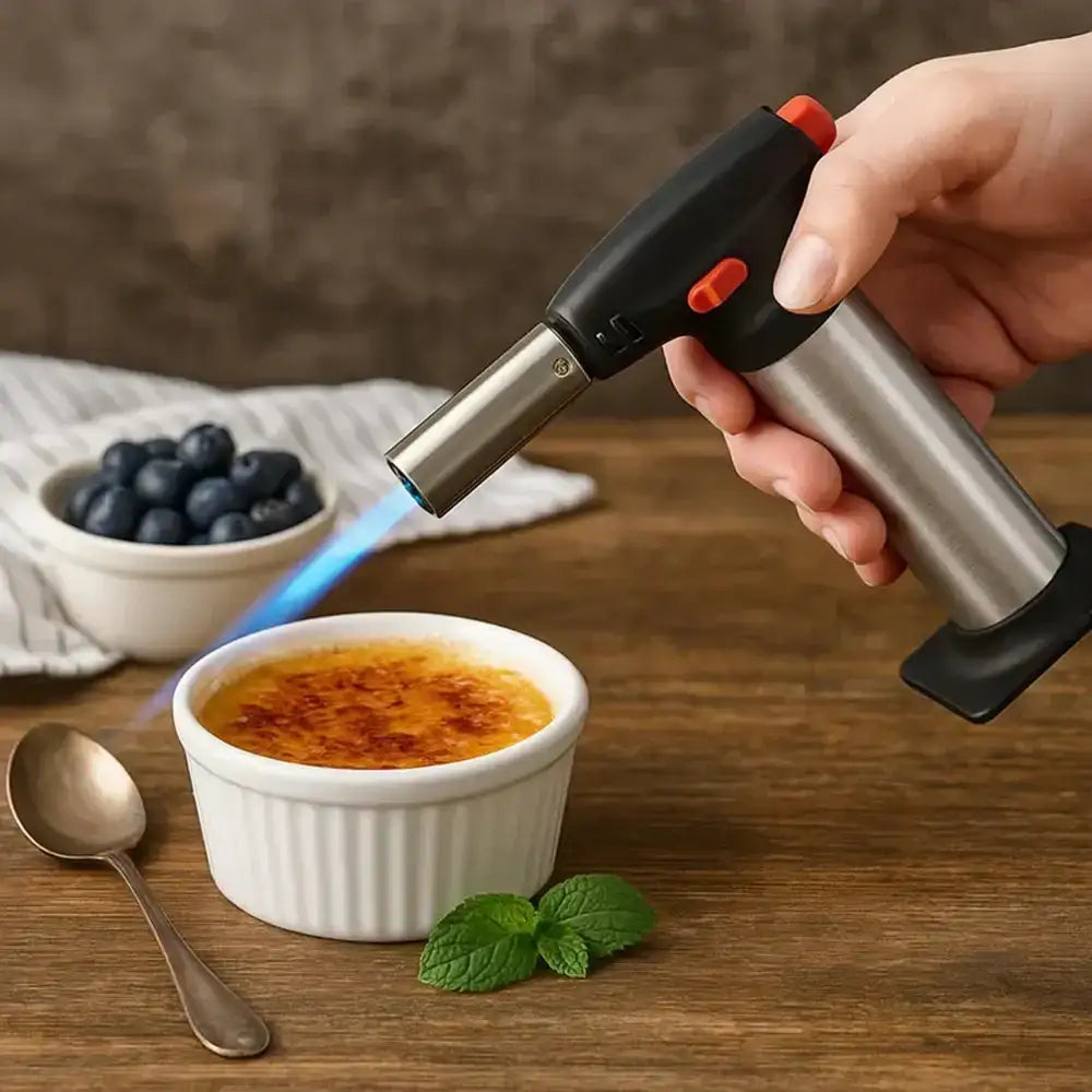 Person using a butane torch to caramelize a dessert on a wooden table with a bowl of blueberries in the background.
