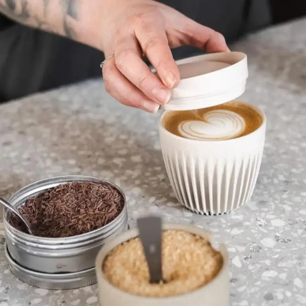 Person holding a lid over a cup of coffee with latte art on a speckled countertop.