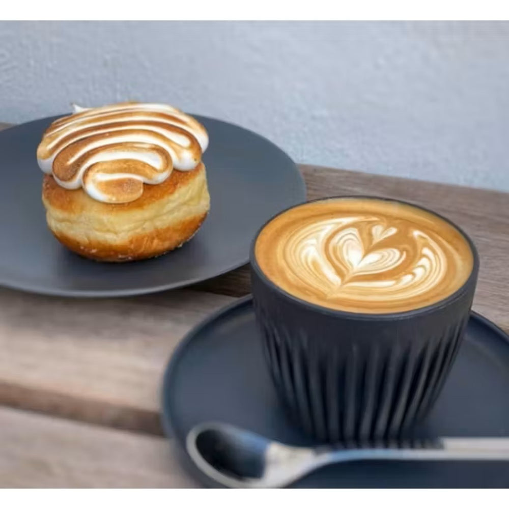 Cappuccino in a black cup with latte art on a wooden table, accompanied by a pastry.