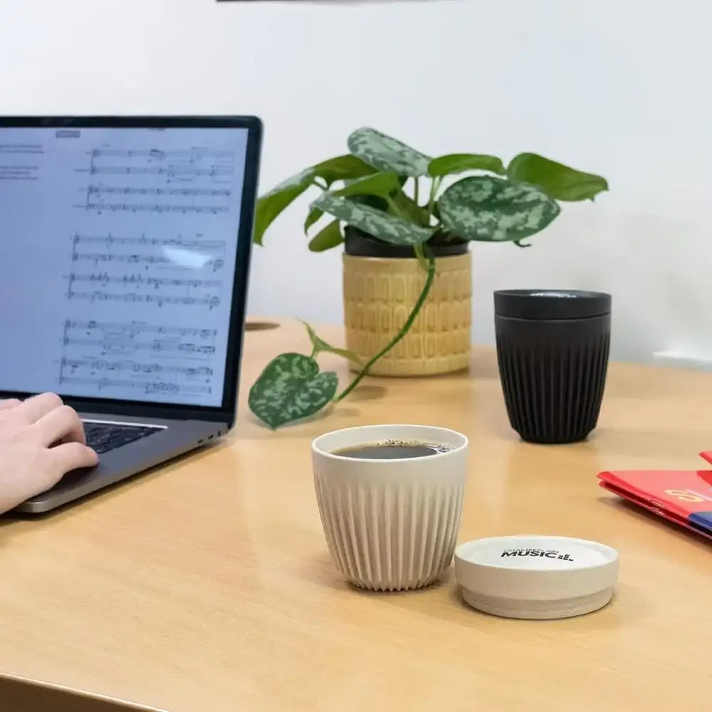 Person working on a laptop with a cup of coffee and plant on a desk