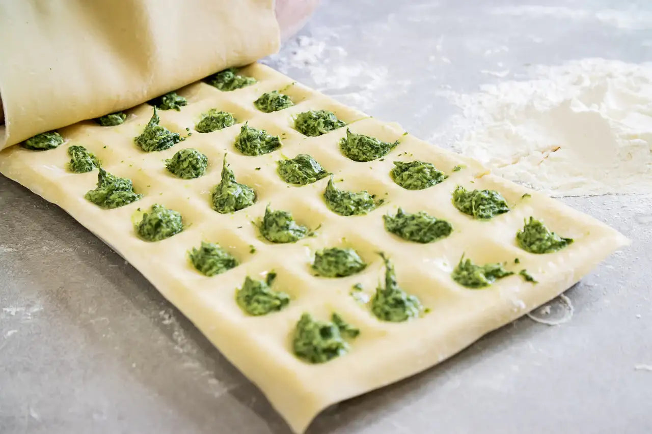 Sheet of dough with green pesto spread across it on a gray surface.