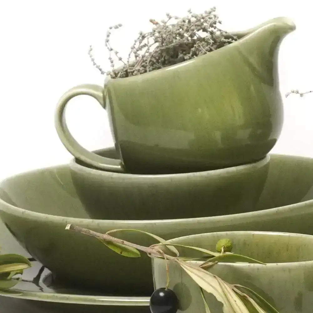 Set of green ceramic dishes with a small plant on a white background