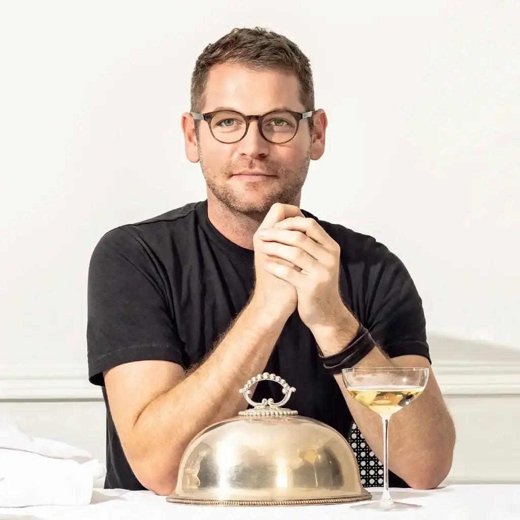 Man sitting at a table with a glass of wine and a covered dish on a white background