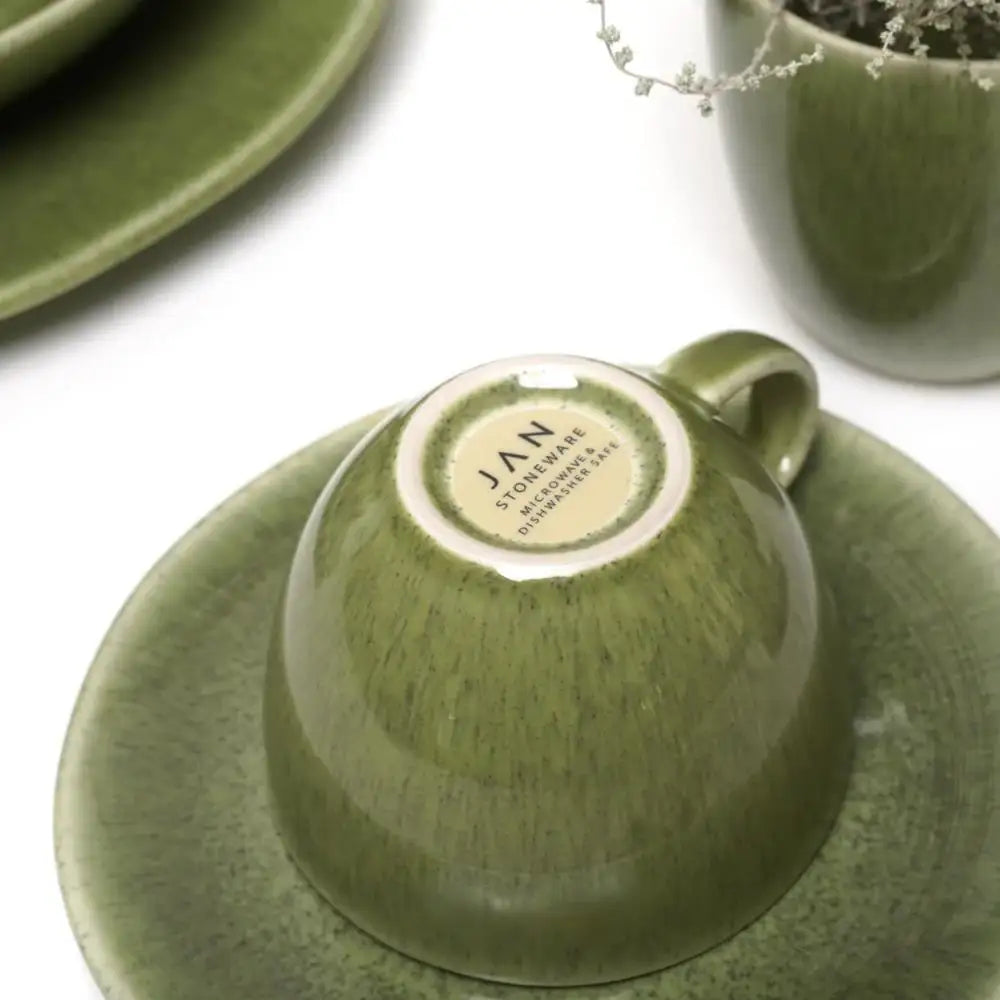 Green ceramic cup and saucer with a visible brand label on a white background