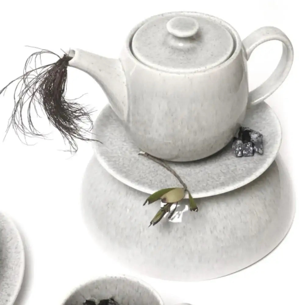 White ceramic teapot and saucer set with tea leaves on a white background