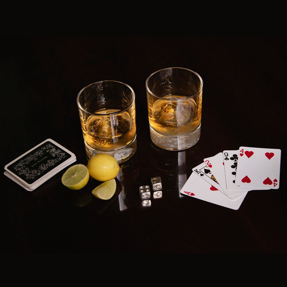 Two glasses of whiskey with lemon slices, playing cards, and dice on a dark surface.
