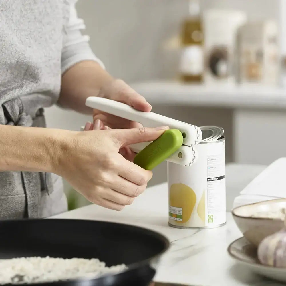 Person using a can opener on a can with a kitchen setting in the background