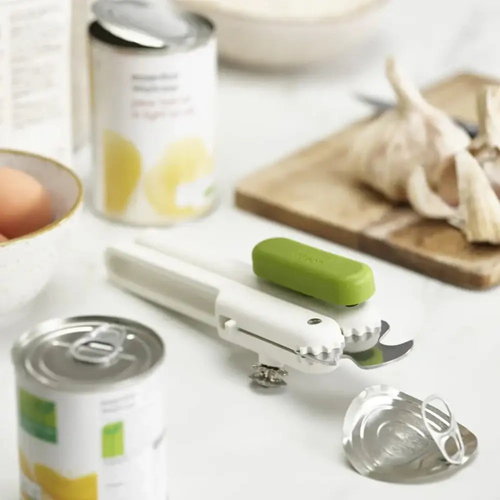Can opener with a green handle on a kitchen counter with food items.