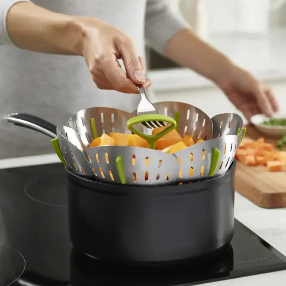 Person using a kitchen tool to stir vegetables in a pot on a stove
