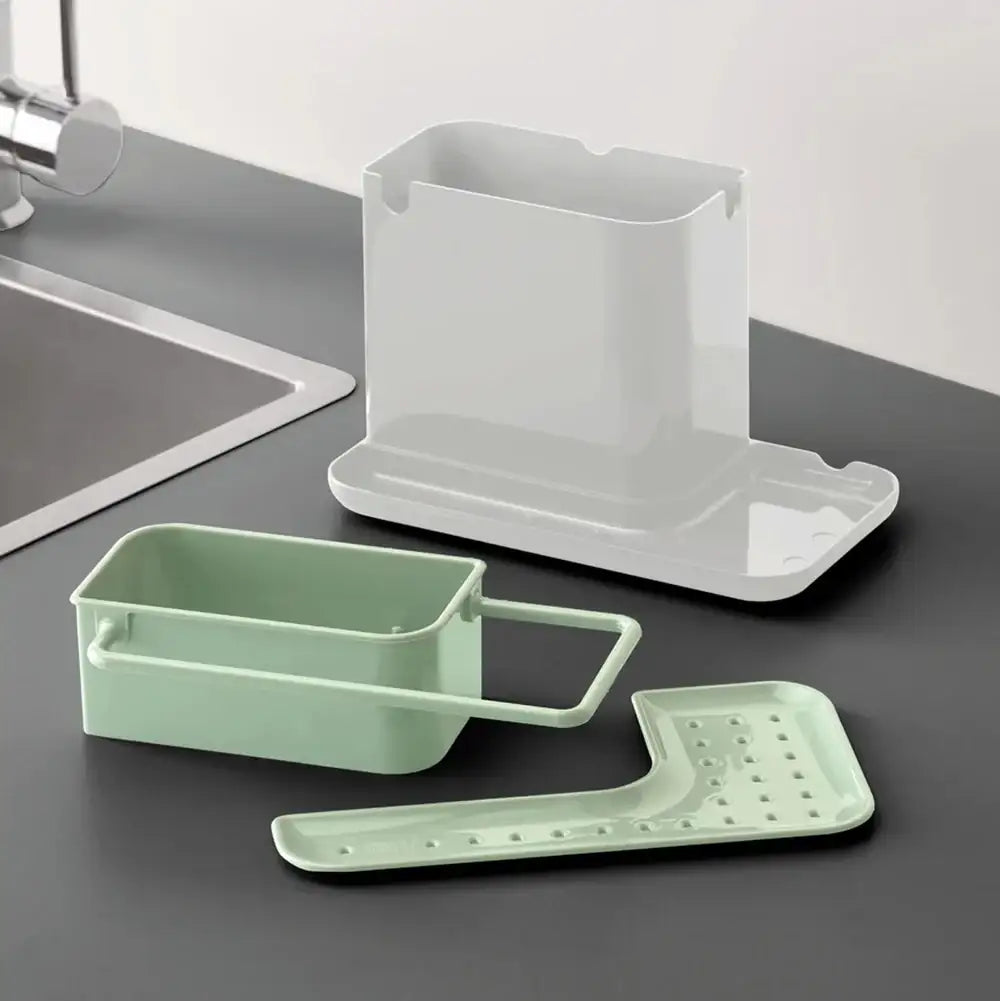 Kitchen sink caddy with green dish drainer and white sponge holder on a dark countertop.