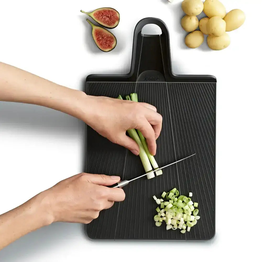 Person cutting vegetables on a black cutting board with figs and potatoes in the background.