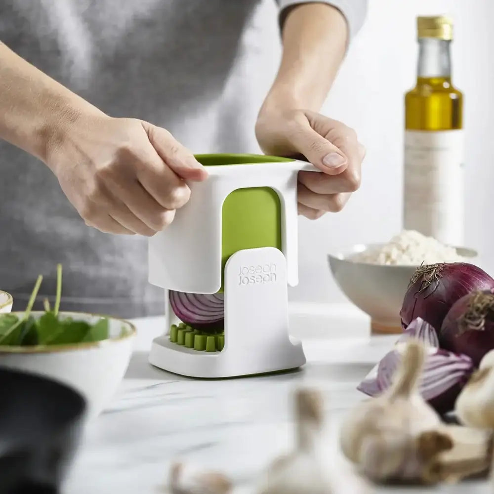 Person using a kitchen tool to slice onions on a countertop with ingredients in the background.