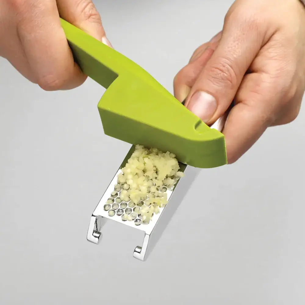 Green garlic press with minced garlic on a gray background