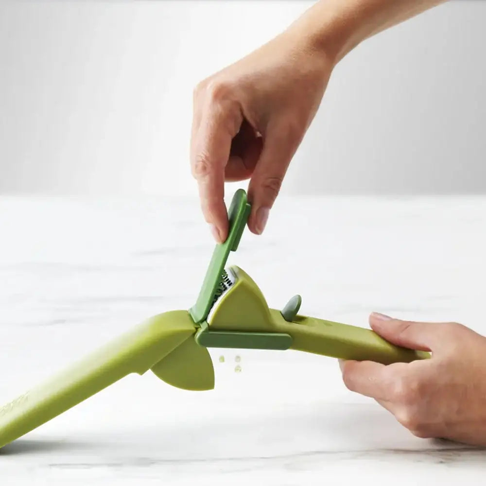 Green kitchen tool being used to grate a vegetable on a white background