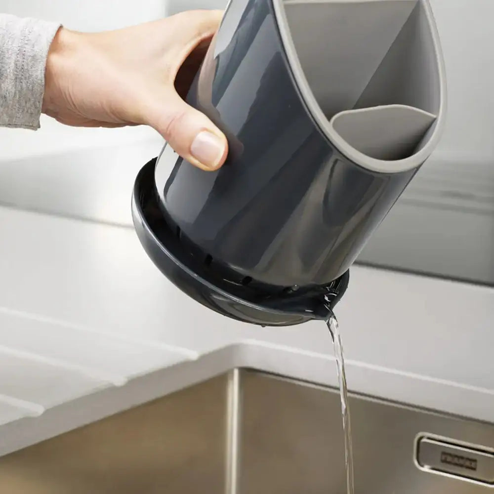 Person pouring water from a black and gray container into a sink.