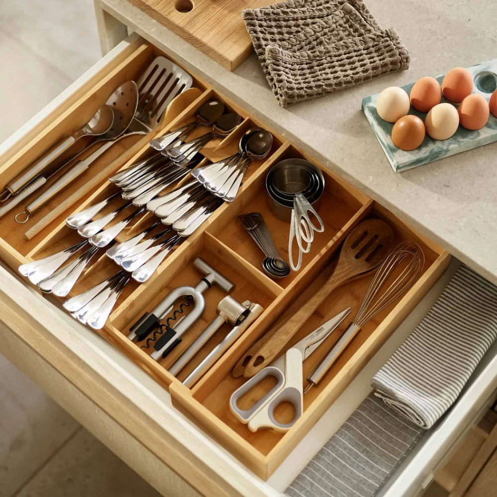 Wooden kitchen drawer organizer with cutlery and utensils on a kitchen counter.