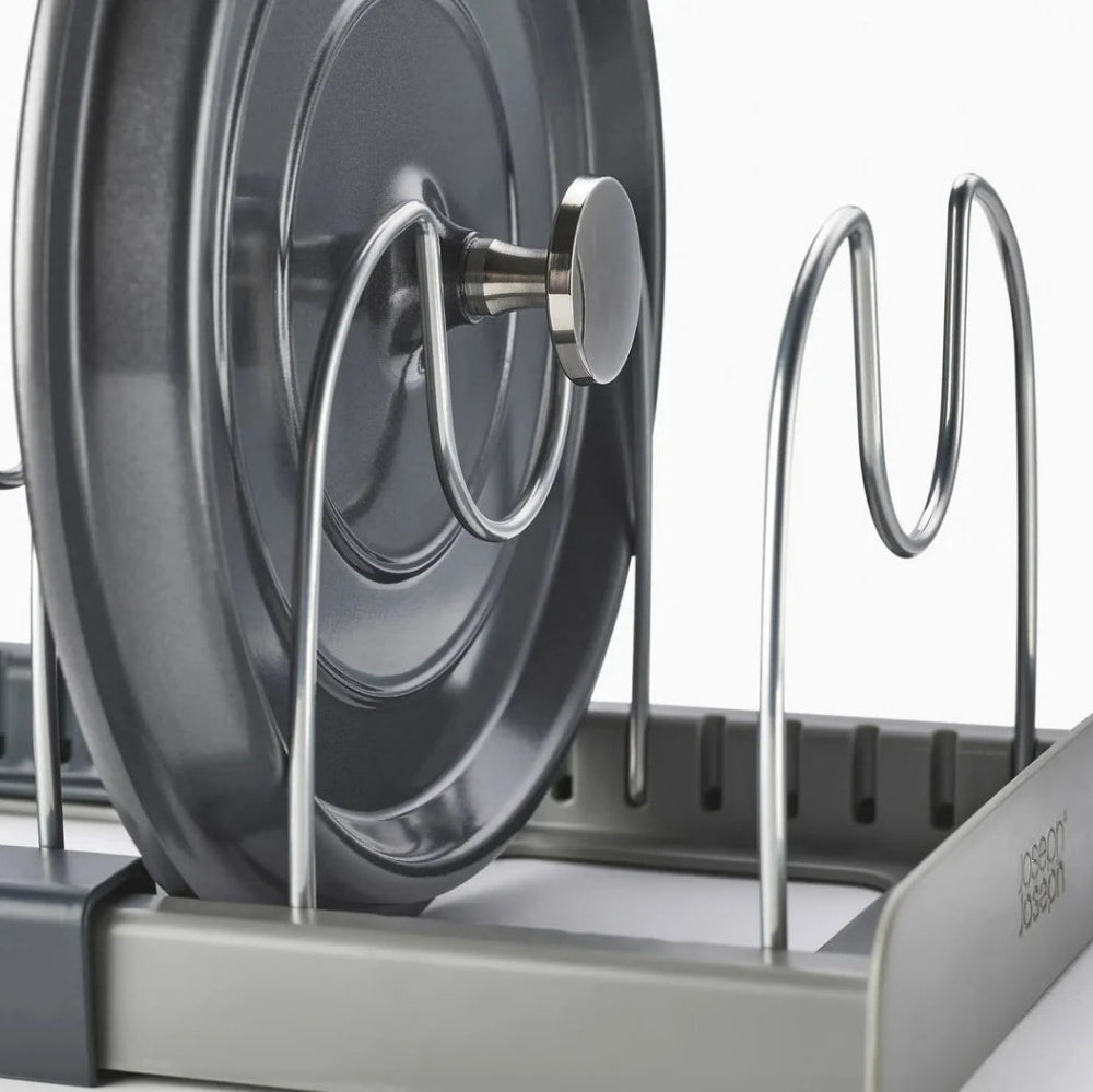 Close-up of a kitchen utensil holder with a dark gray round pan or lid leaning in the center.