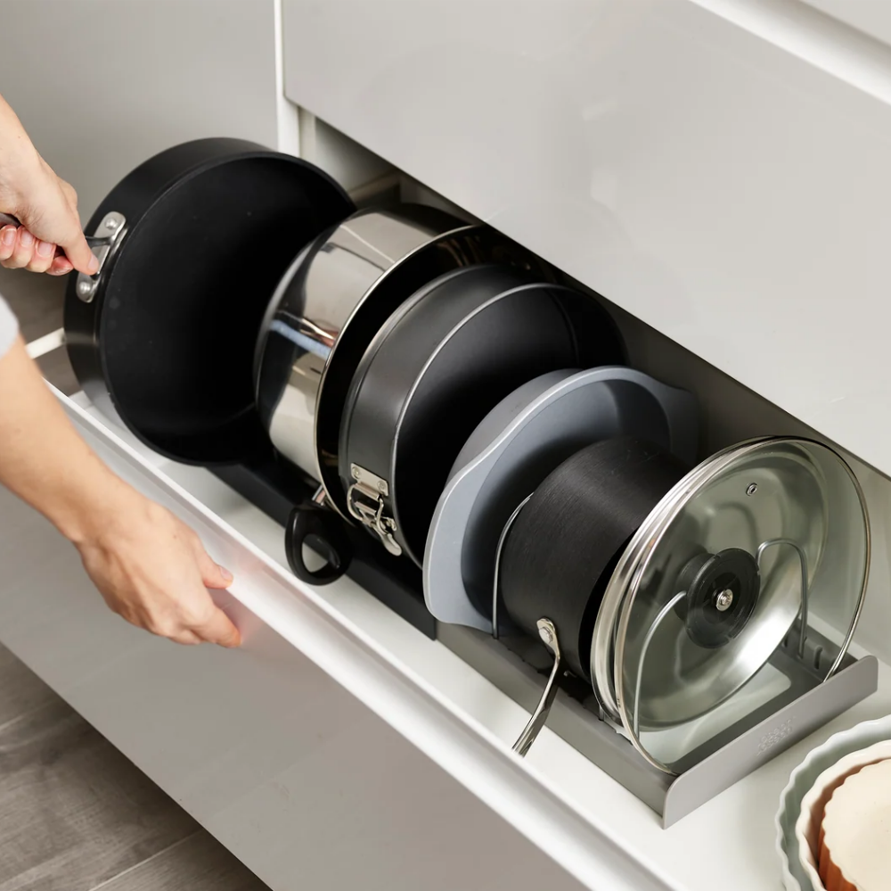 Stack of pots and pans in a kitchen drawer with a person's hand opening it.