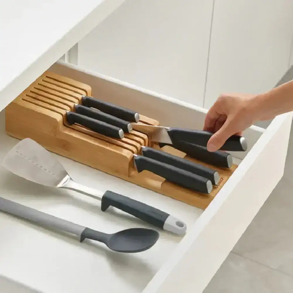 Set of knives with black handles in a wooden block on a kitchen counter.