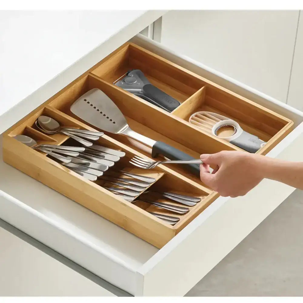 Wooden kitchen utensil organizer with cutlery and a hand reaching in to pick up a fork.